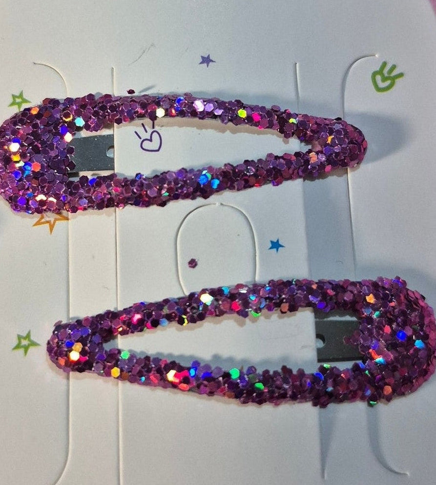 Purple glittery hair clips on a white card with a pink bow design, placed on pink straw-like material.