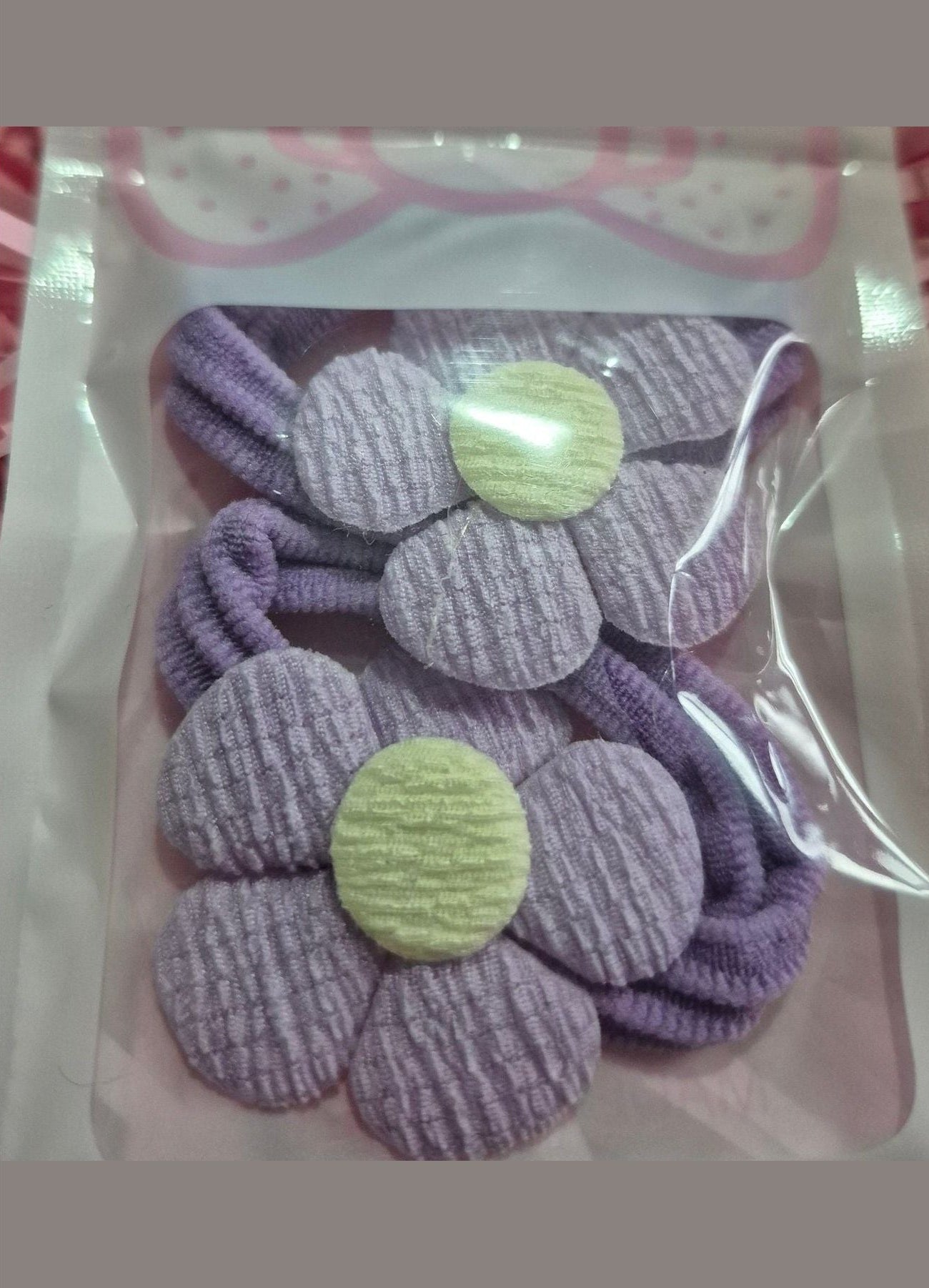 Set of purple flower-shaped hair ties in clear packaging on a pink textured background