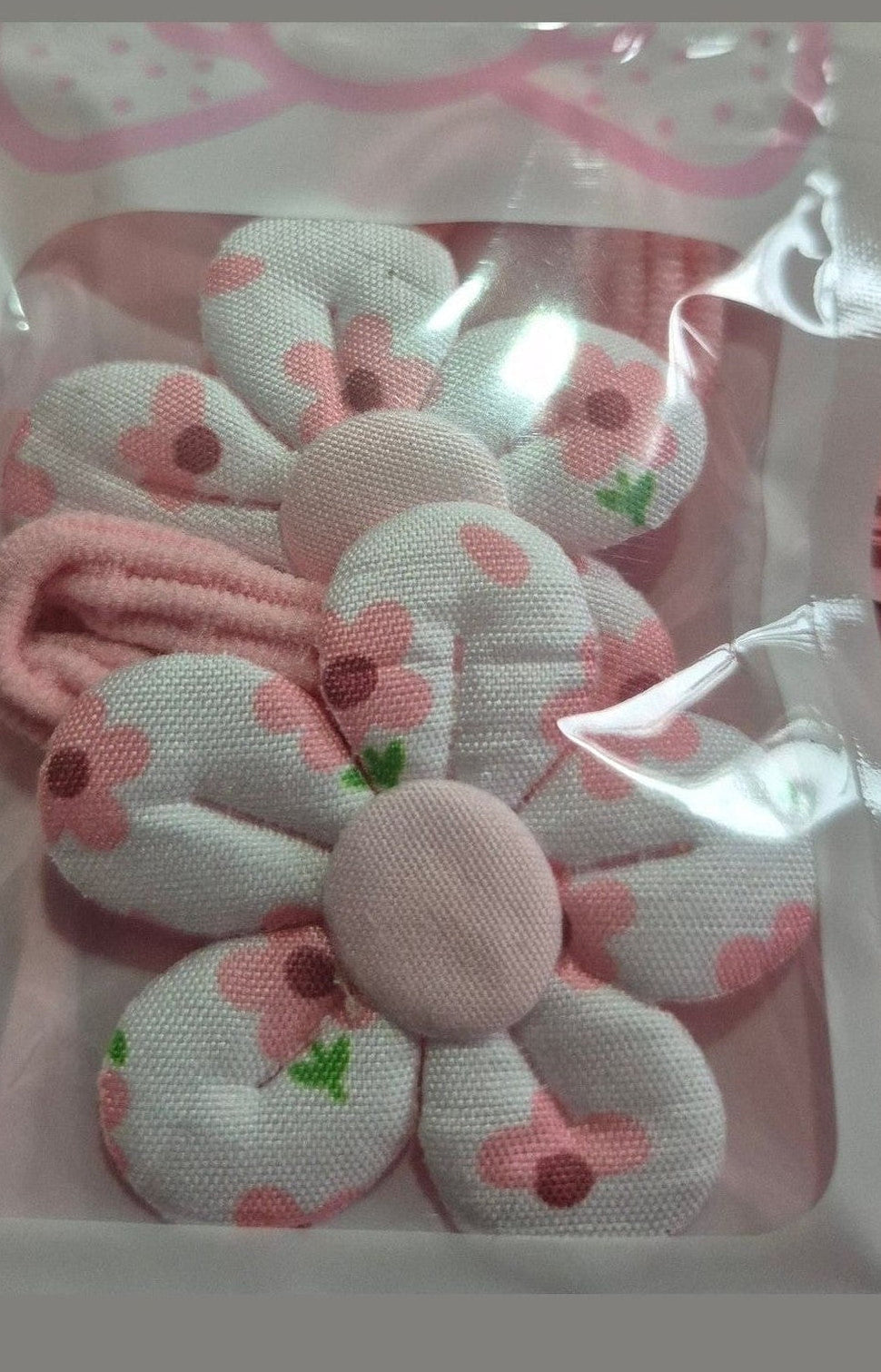 Set of pink hair ties with floral designs in a clear plastic package on a pink background.