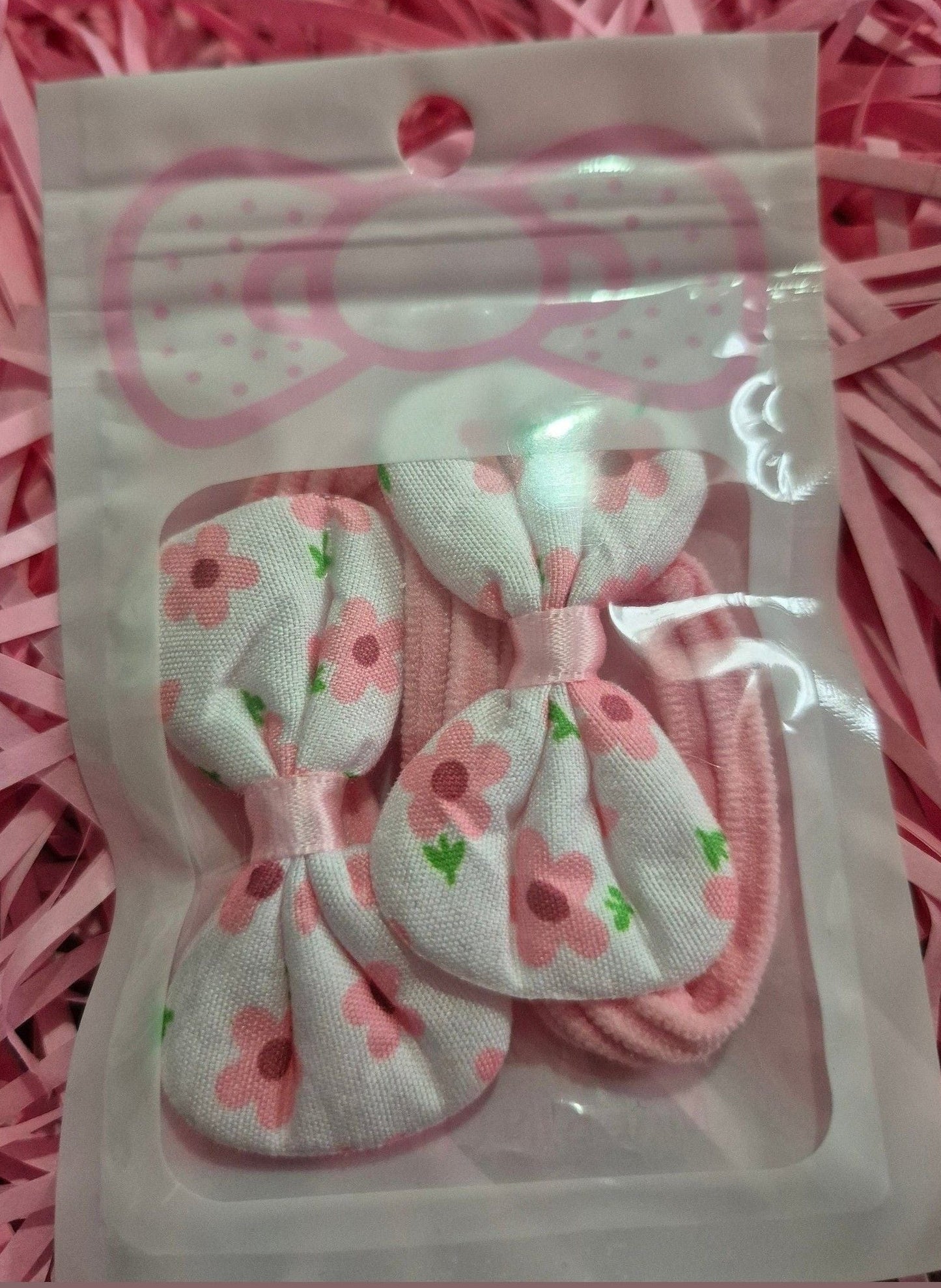 Set of pink and white hair bows with floral patterns in a clear package on a pink background.