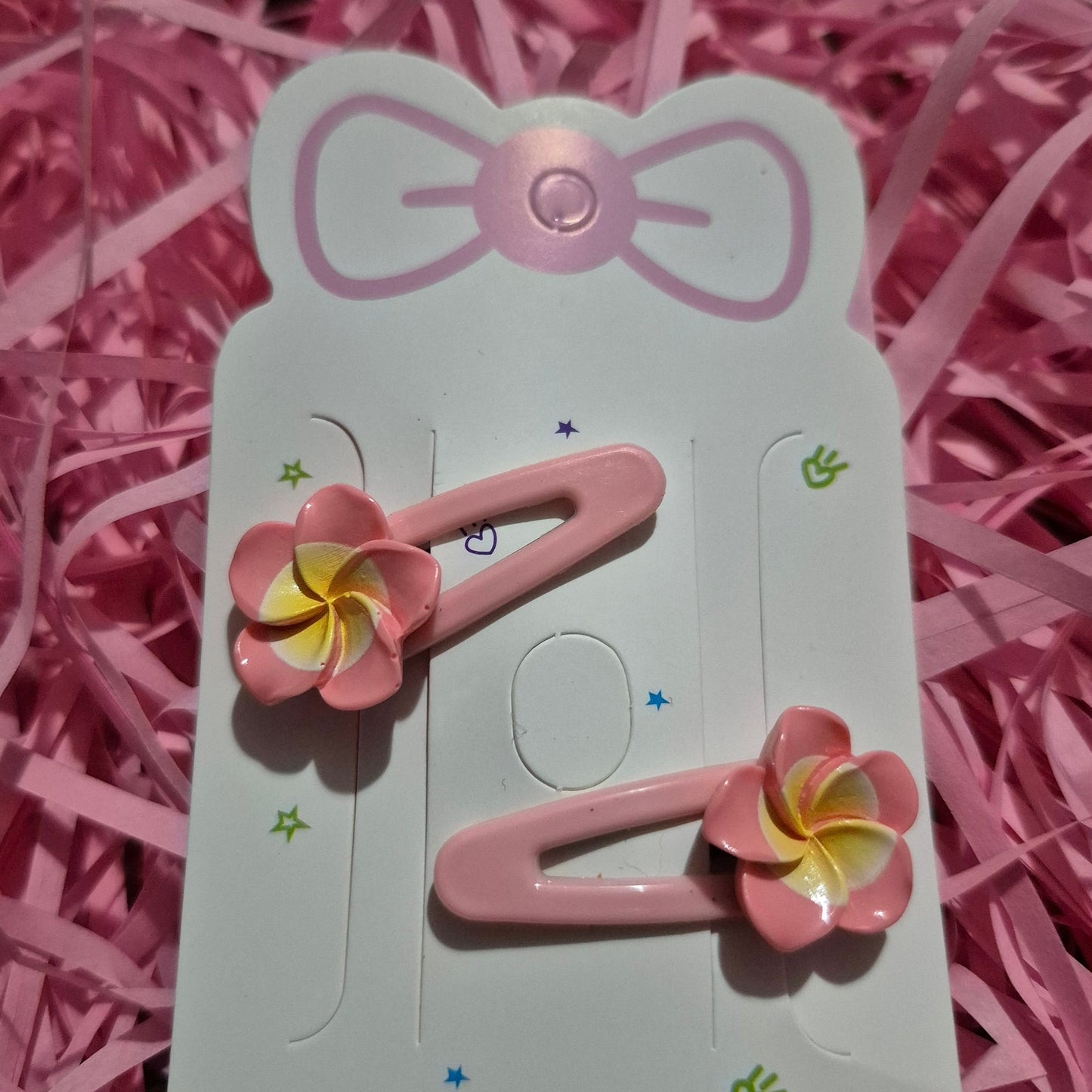 Pink hair clips with floral designs on a white card against a pink shredded paper background