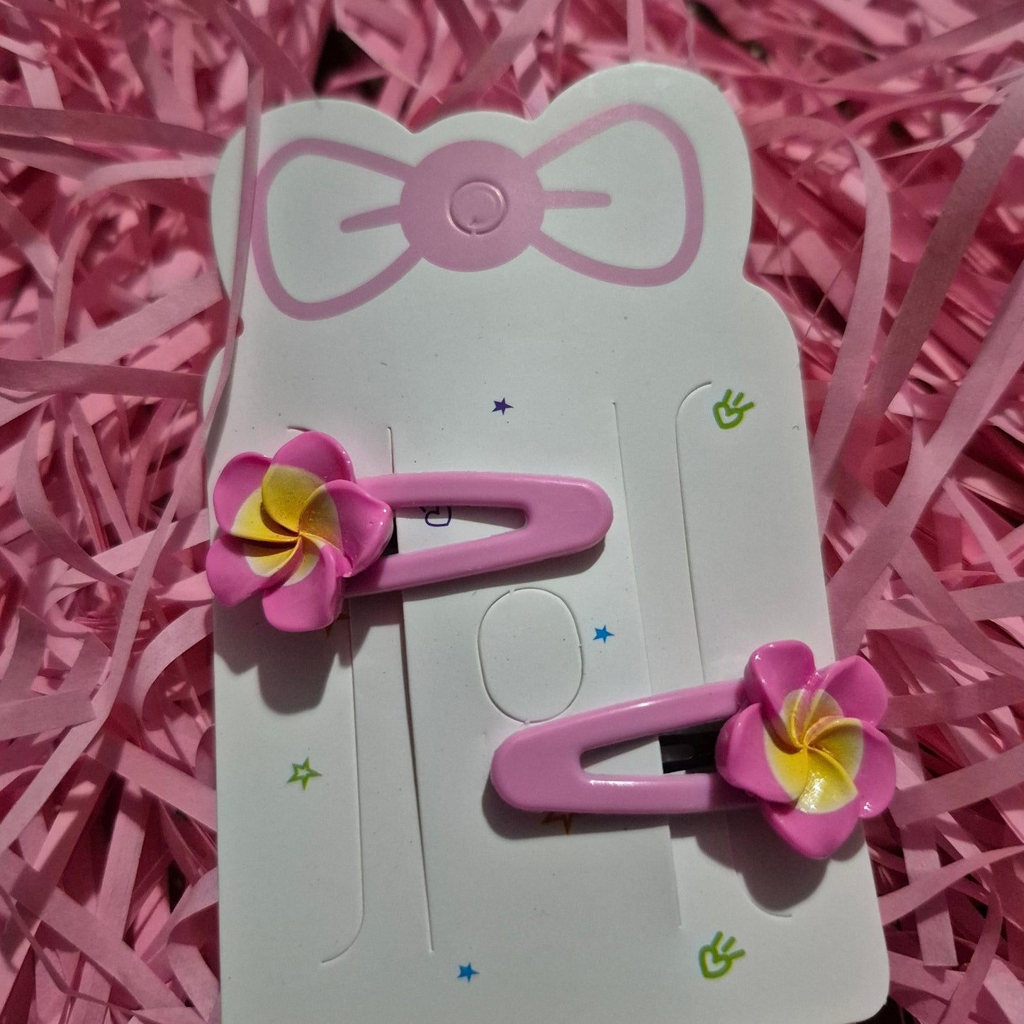 Pink hair clips with flower designs on a white card, placed on pink shredded paper.