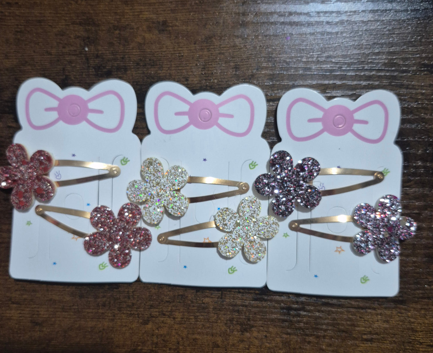 Three sets of decorative hair clips with flowers and bows on a wooden surface.