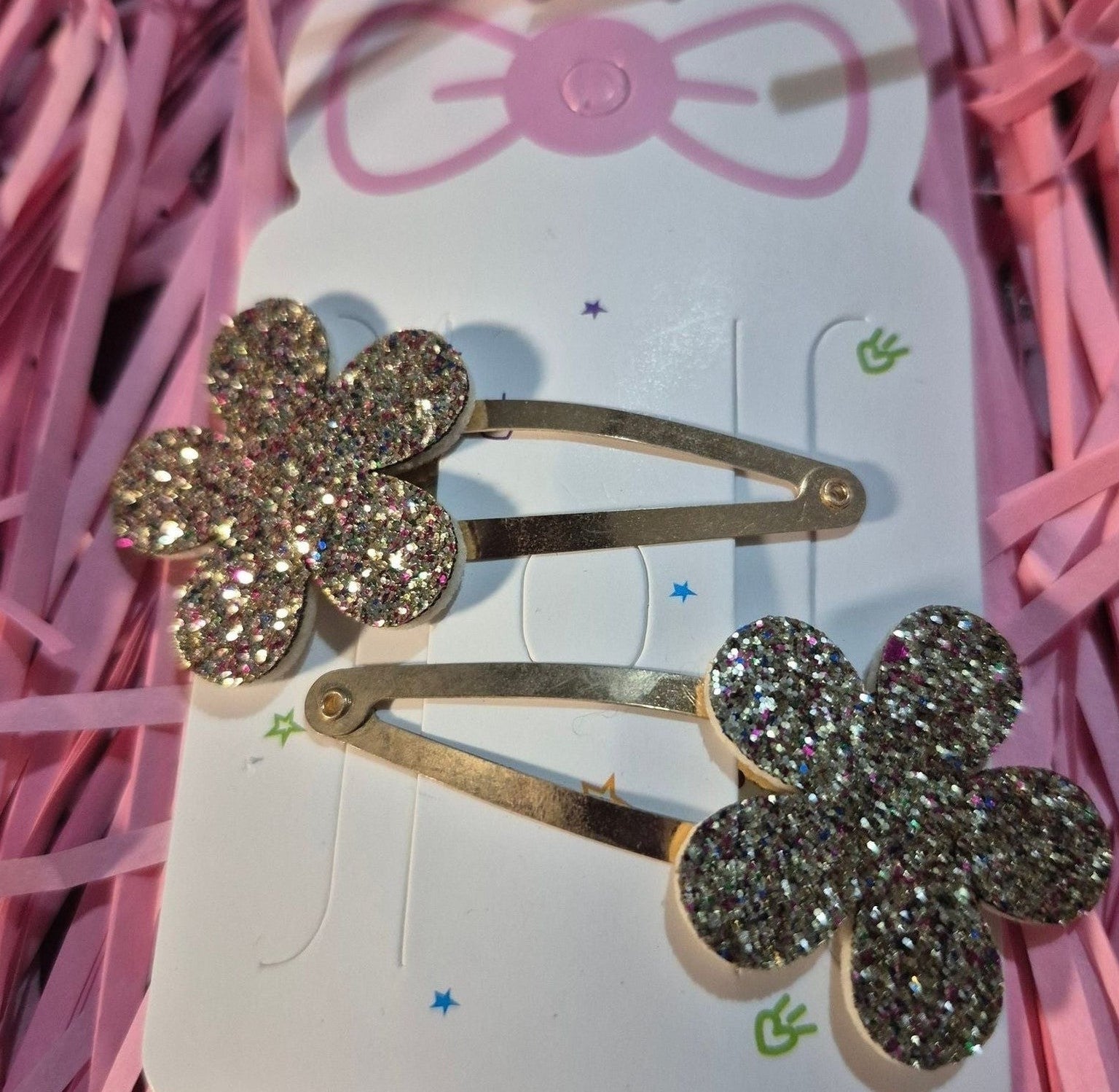 Two gold flower-shaped hair clips on a pink ribbon background