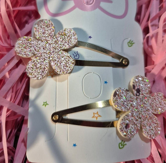 Two decorative hair clips with floral designs on a pink background