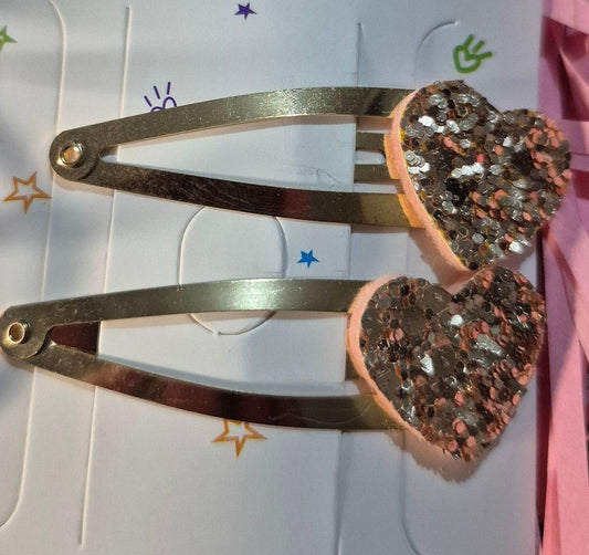 Heart-shaped hair clips on a pink and white card with a bow design, against a pink straw background.