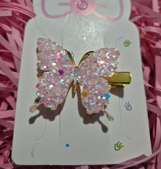 Butterfly-shaped hair clip with rhinestones on a pink card with a bow, set against pink shredded paper.