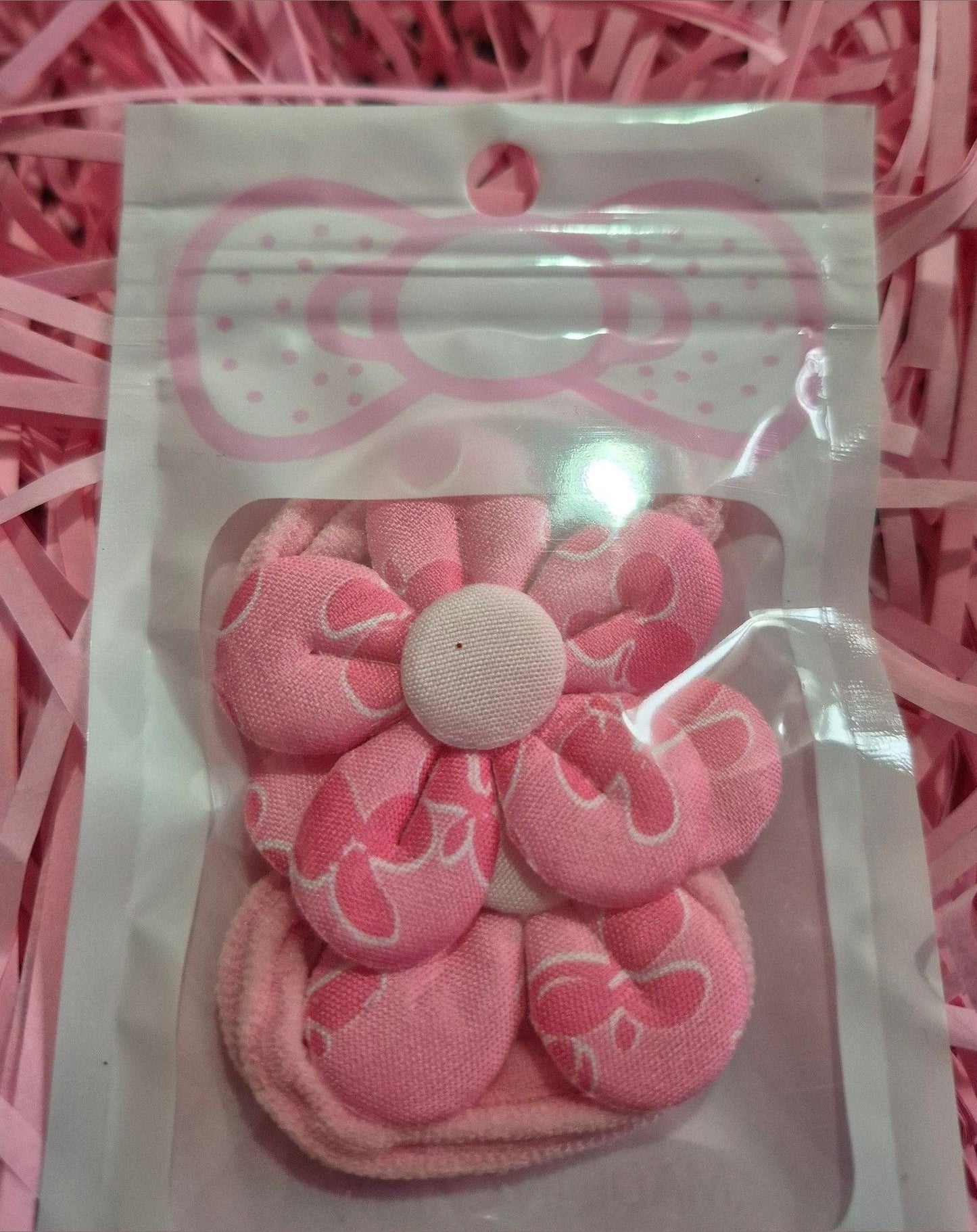 Pink hair ties with a decorative bow in a clear package on pink shredded paper.