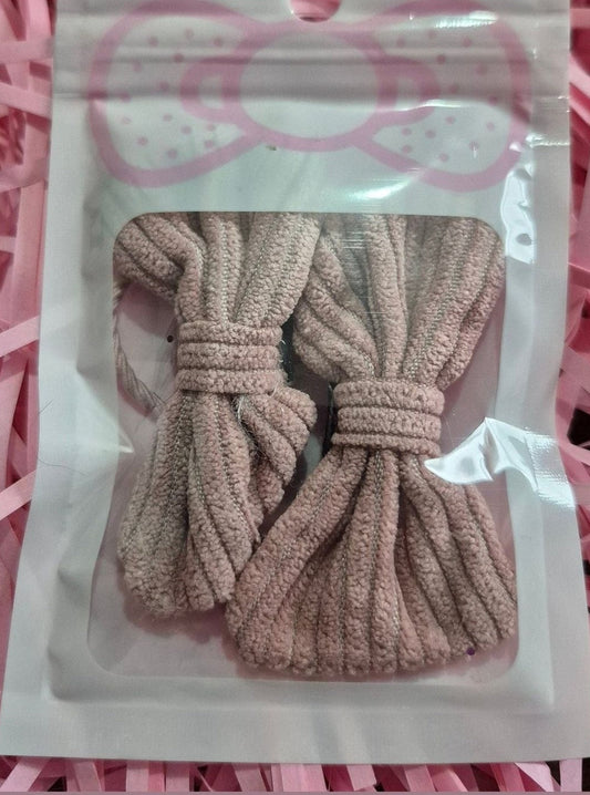 Two beige hair ties in a clear plastic bag on pink crinkled paper