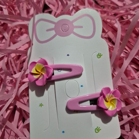 Pink hair clips with flower designs on a white card, placed on pink shredded paper.