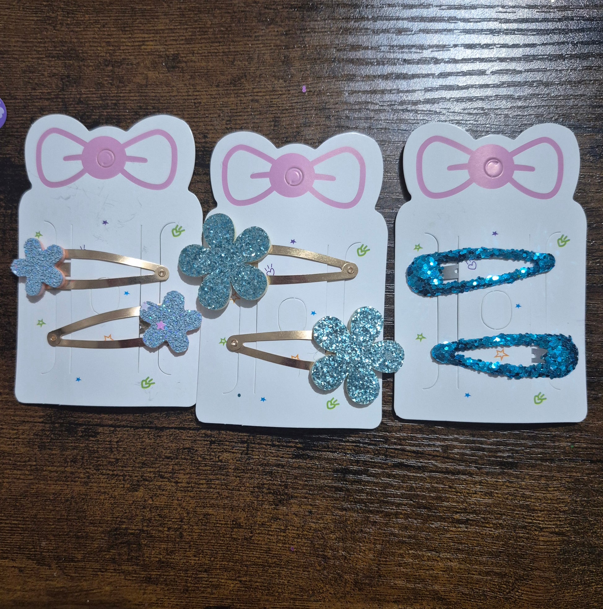 Three packages of hair clips with floral designs on a wooden surface