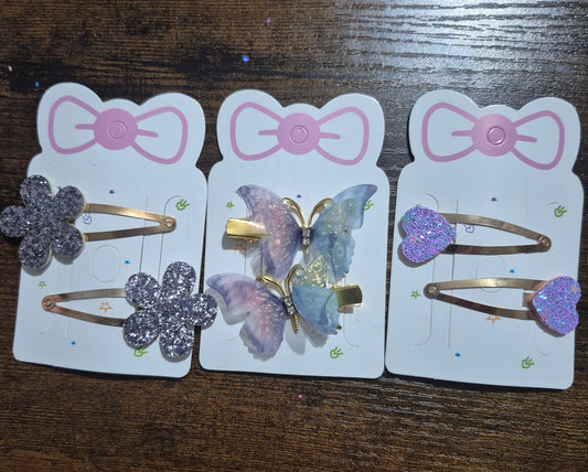 Three packages of hair accessories with butterfly and flower designs on a wooden surface.