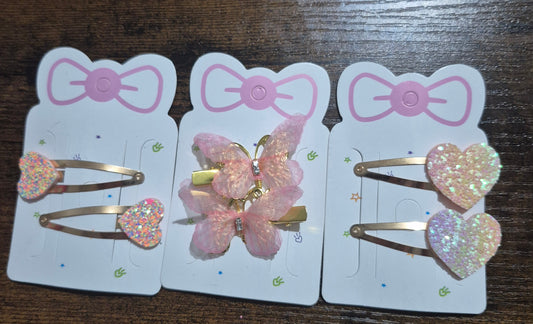 Three hair clips with pink bows on cards against a dark surface