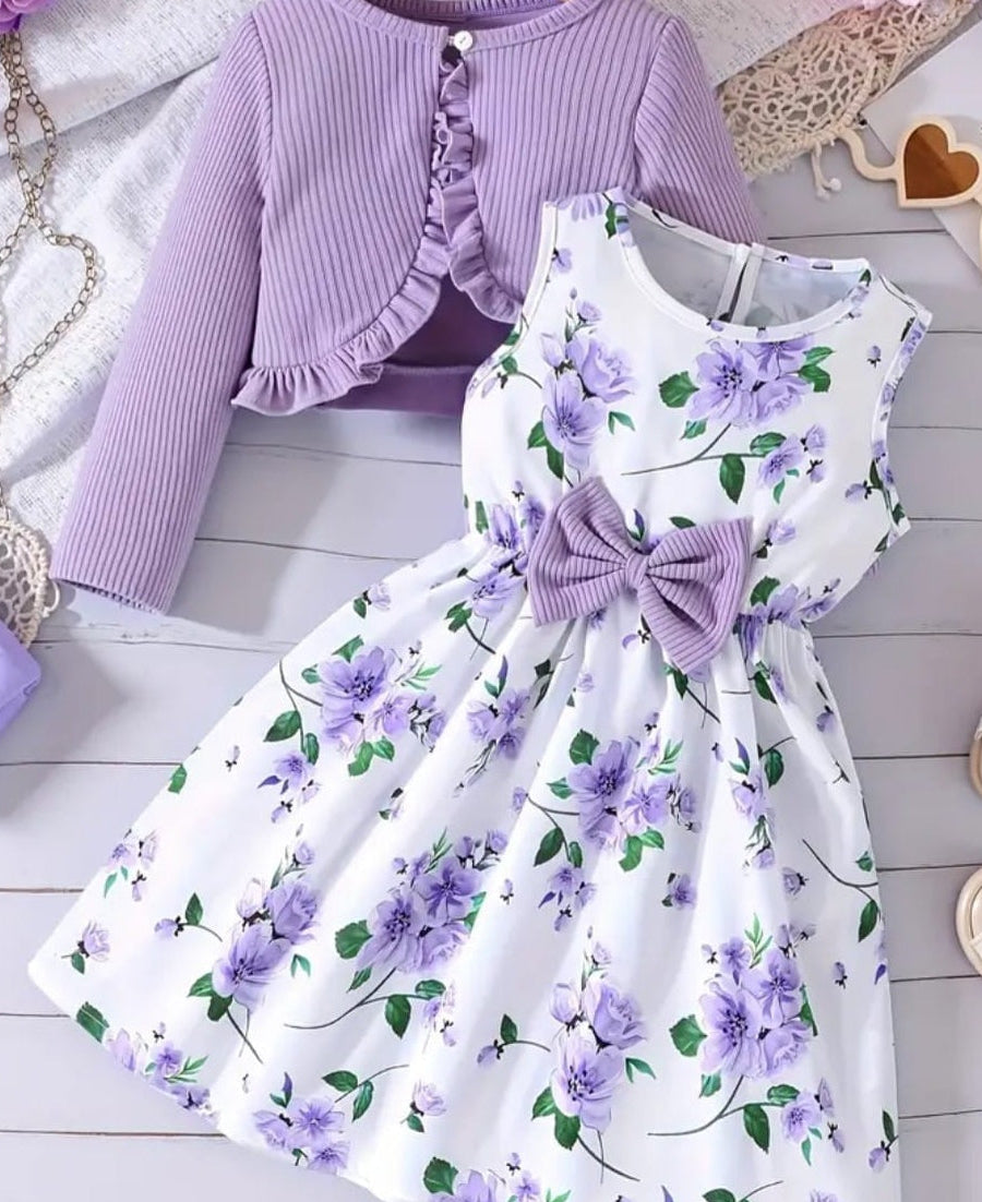 Children's outfit with a purple cardigan and floral dress on a wooden floor.