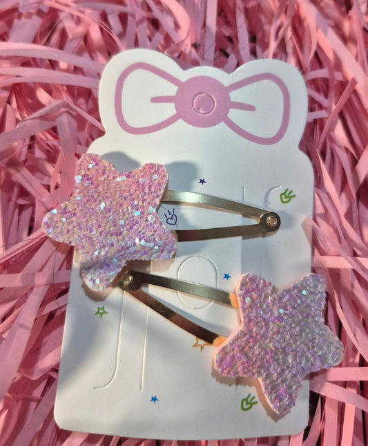 Star-shaped hair clips on a white card with a pink bow design, set against a pink shredded paper background.